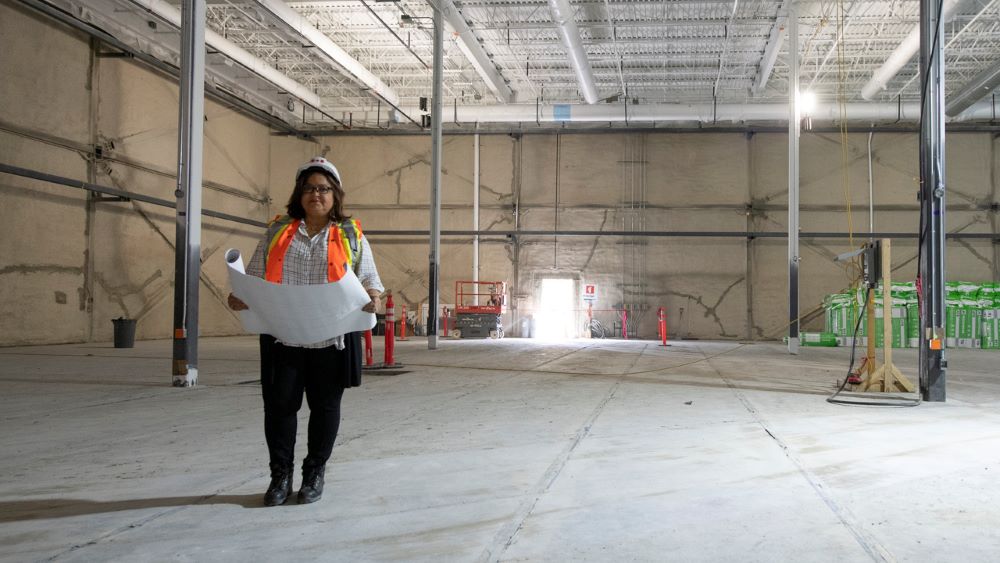 A project manager in a helmet standing in a large, empty space under construction.
