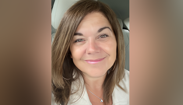 Une femme souriante aux longs cheveux bruns qui porte un chemisier blanc.