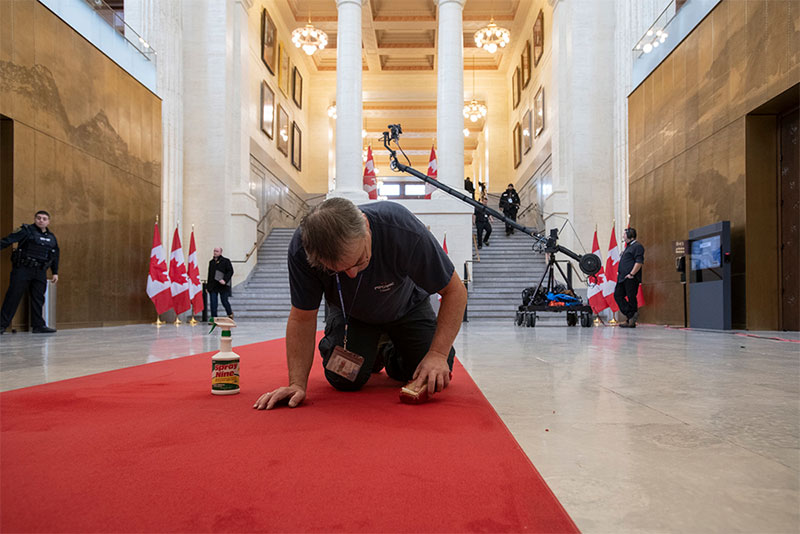 An employee scrubbing out a stain on a red carpet in the Senate of Canada entrance
