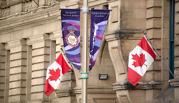 Jubilee and Canadian flags on a flag pole in front of a building.