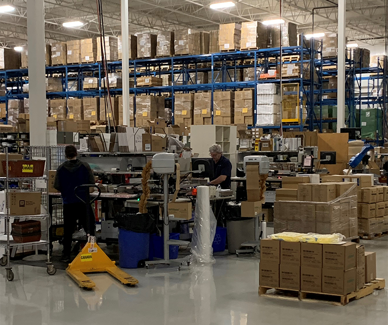 People are working in a warehouse where there are many shelves packed with boxes.