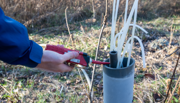 A person's hand is holding a tool next to a pipe with some plastic tubes.