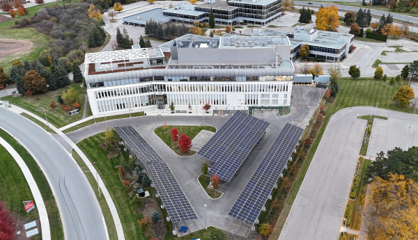 Vue aérienne d'un immeuble de laboratoire blanc avec des panneaux solaires au-dessus de l'aire de stationnement entourés de feuillages d'automne.