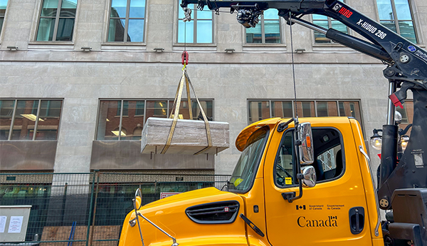 A yellow mobile crane truck in front of a modern concrete building.