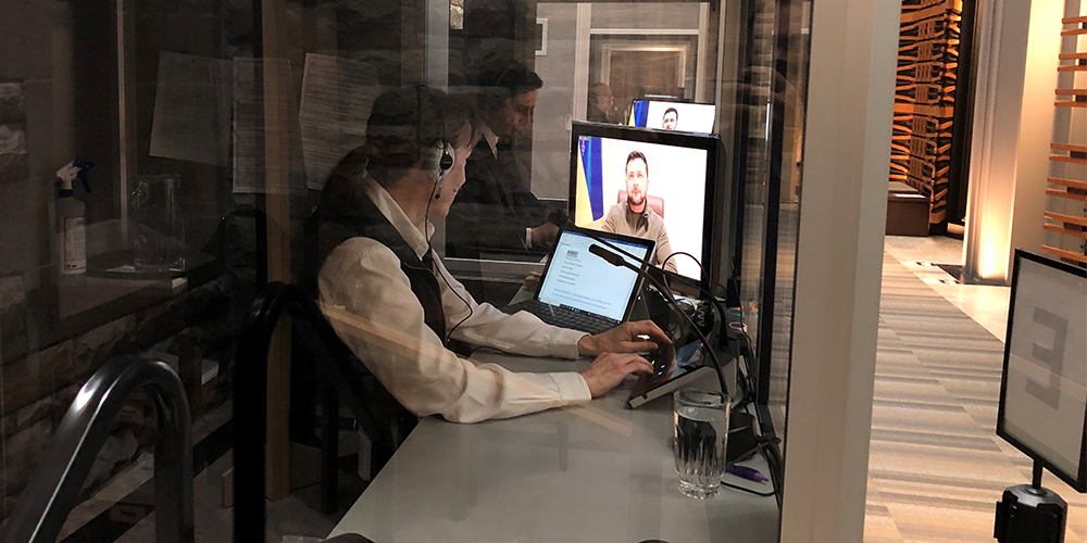 Marie-Ève Racette, with headphones, seen from behind sitting in a glass cubicle in front of computer screens.