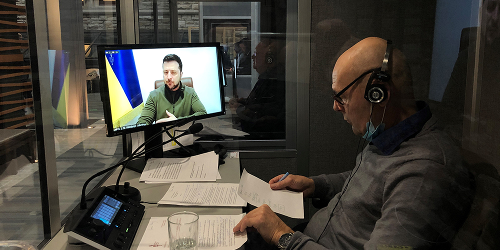 Vasili Kosenko, avec écouteurs, vu de côté assis dans un cubicule en verre tenant des documents en papier.