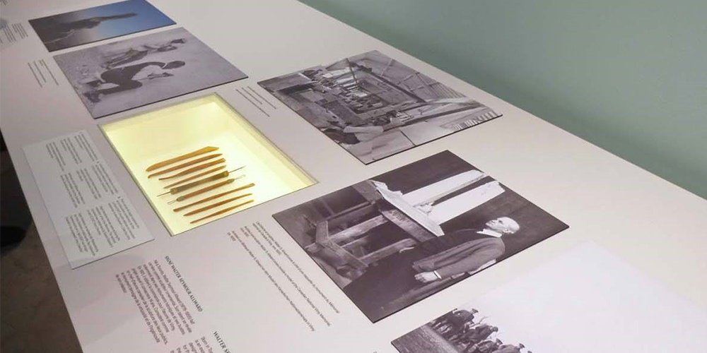 Une exposition présentant des photos en noir et blanc, ainsi que des artefacts dans une vitrine éclairée.