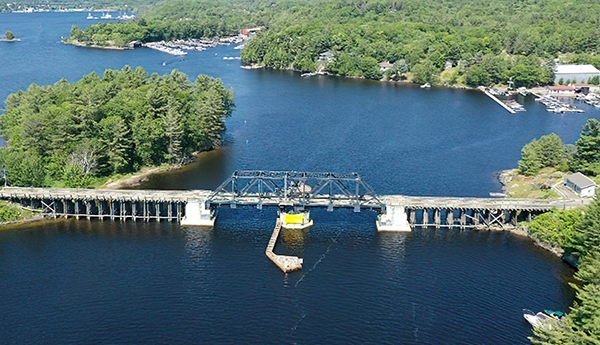 Aerial view of a closed swing bridge with a lake and trees in the background.