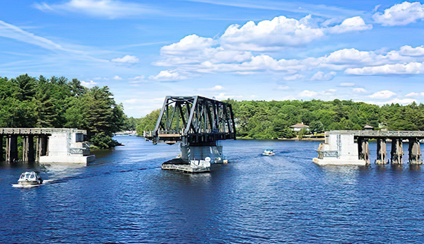 A lake with an open swing bridge and boats passing through. There are trees in the background.