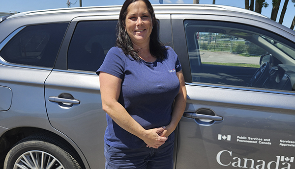 Woman wearing blue apparel standing in front of a vehicle marked with the 'Canada' watermark with trees and utility poles in the background.