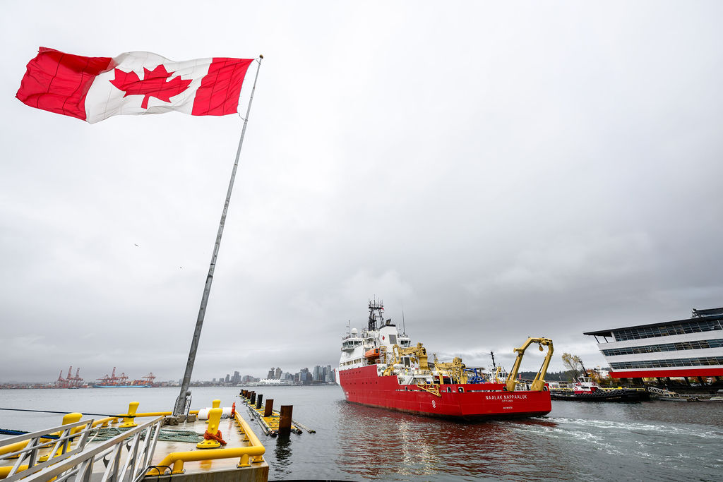 A large red and white ship sailing near a dock with a Canadian flag
