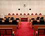 Enlarged image of the Modern courtroom featuring a judges’ bench, counsel tables, public seating, red carpeting, and tall illuminated wood-panelled walls.