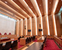 Enlarged image of the Courtroom interior with tiered seating, counsel tables, digital display screens, red carpeting, and a high ceiling with wood panelling and natural light.