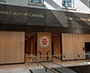 Enlarged image of the Large Supreme Court of Canada emblem mounted on a wood-panelled wall between two entranceways.