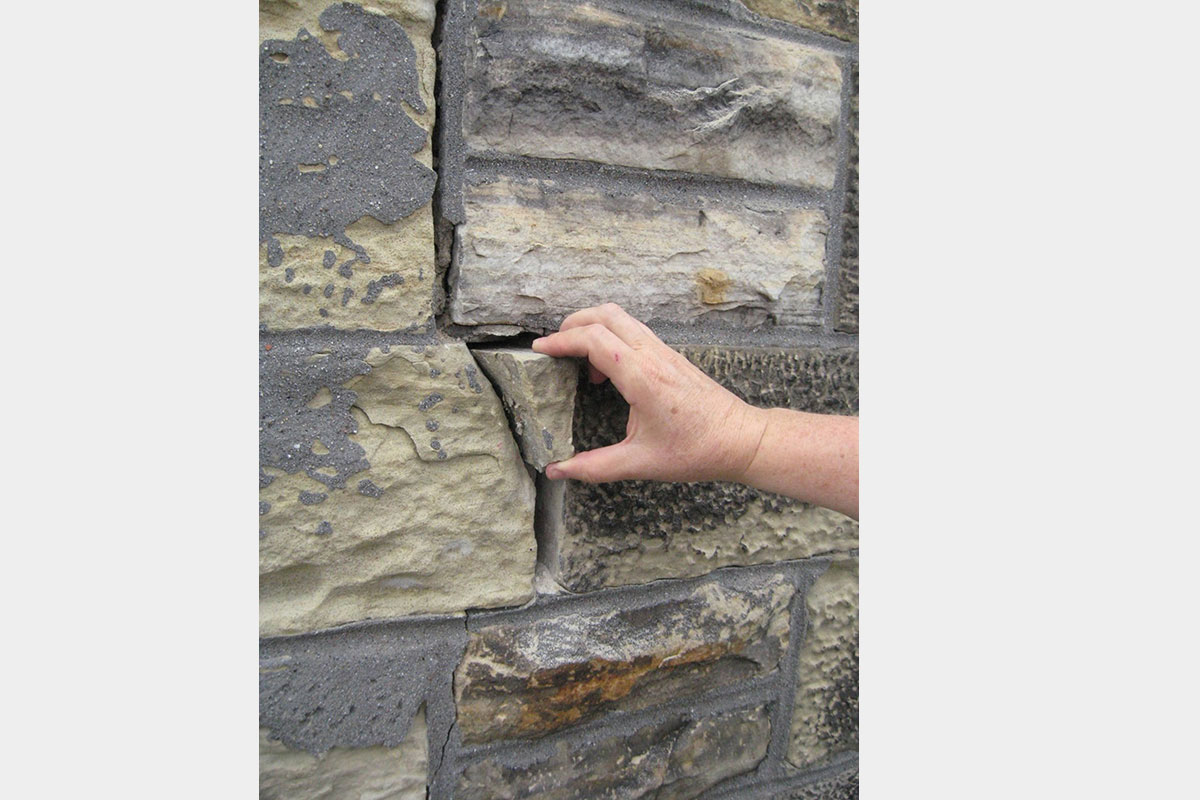 A hand removing a broken piece of stone from a masonry wall.
