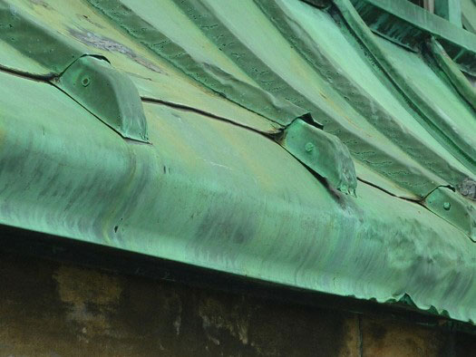 A green copper roof that is dented and damaged.