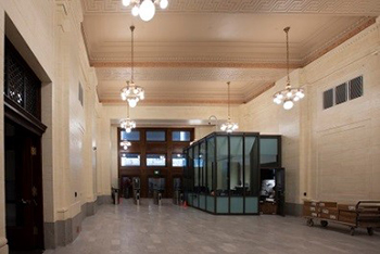A hallway with marble finishes and an intricate ceiling. There is an entranceway at the end of the hallway with security turnstiles and a glass security booth.