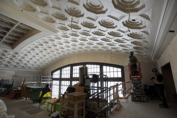 Two workers install lights in a plaster ceiling.