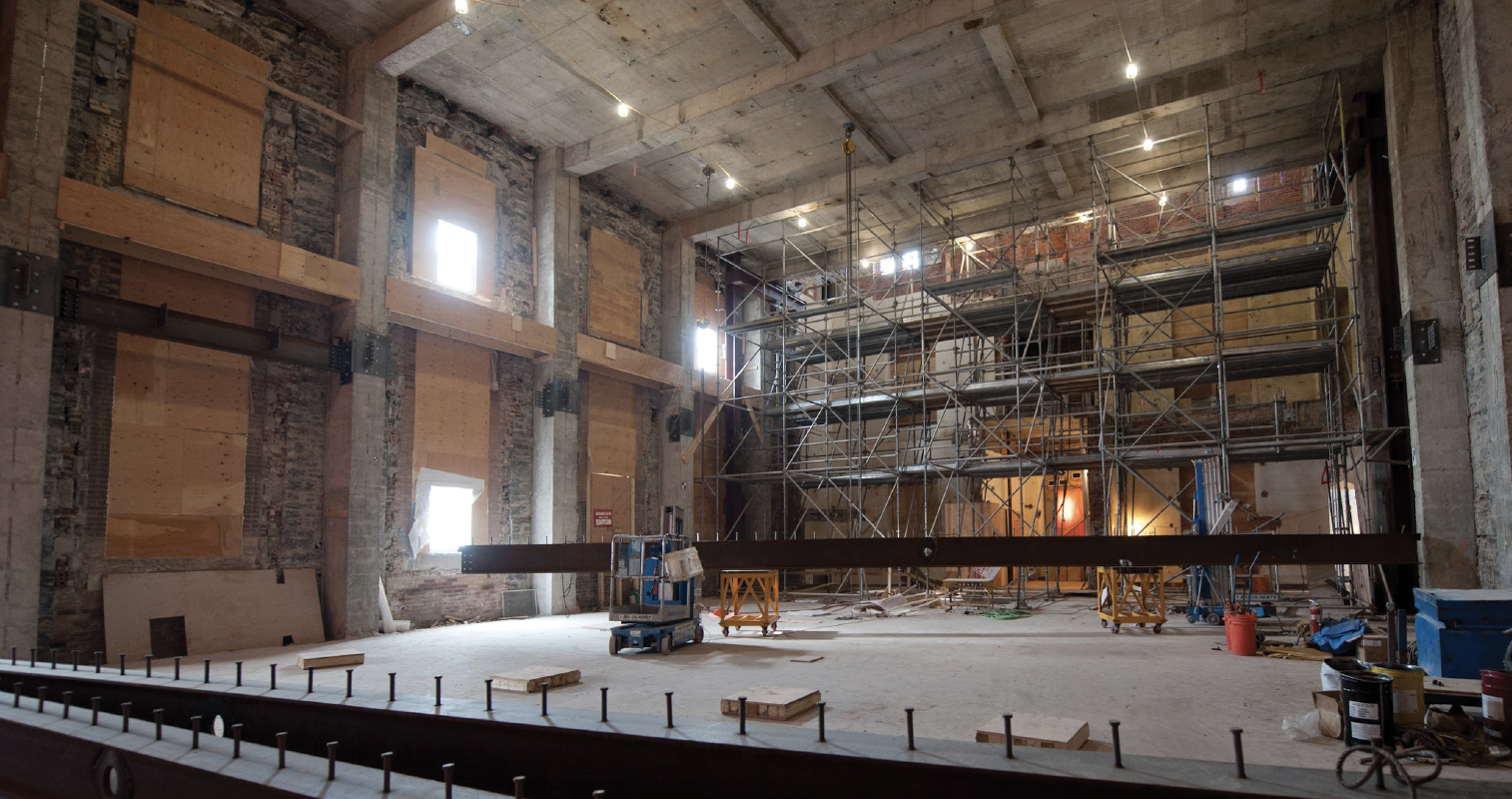 The interior of the historic West Block building is stripped down to its masonry walls and concrete floors. There is scaffolding and construction materials.