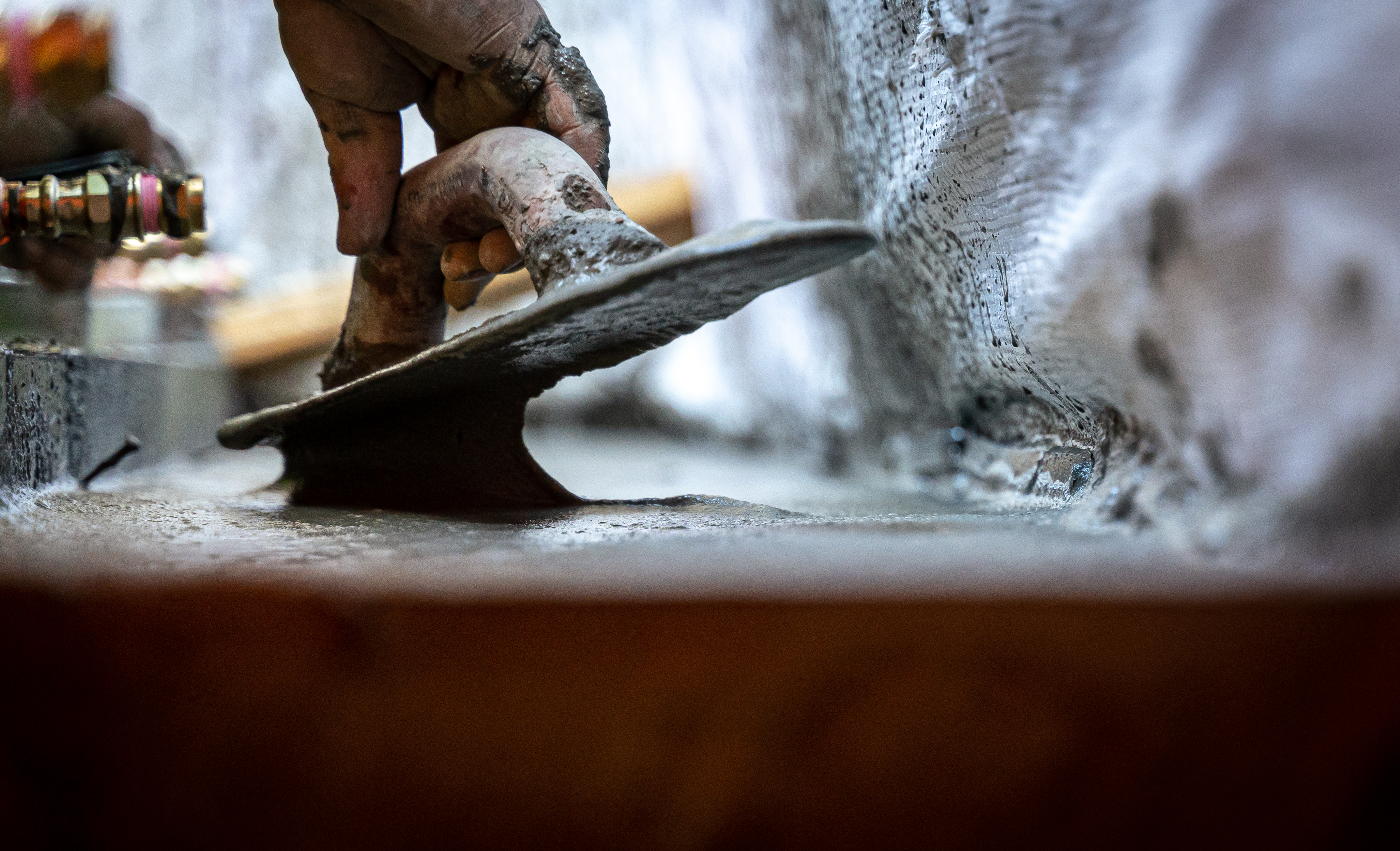 A hand spreads concrete with a trowel.