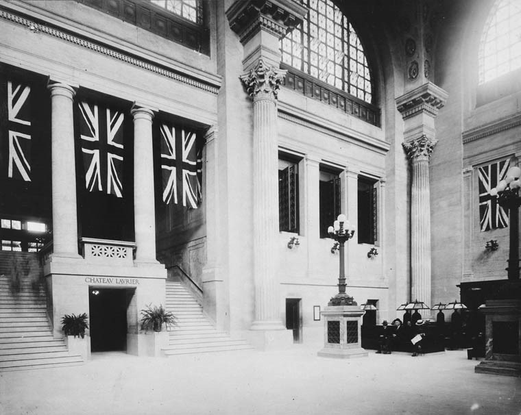 View enlarged image of a black and white photo of a train station with Union Jack flags hung for decoration.