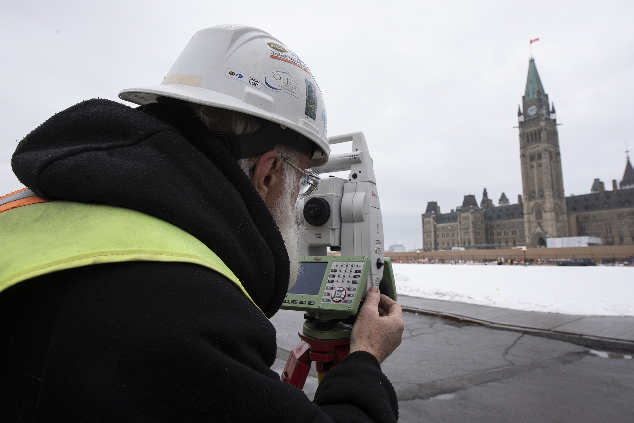 A man looks at a Gothic-style building through surveying equipment.