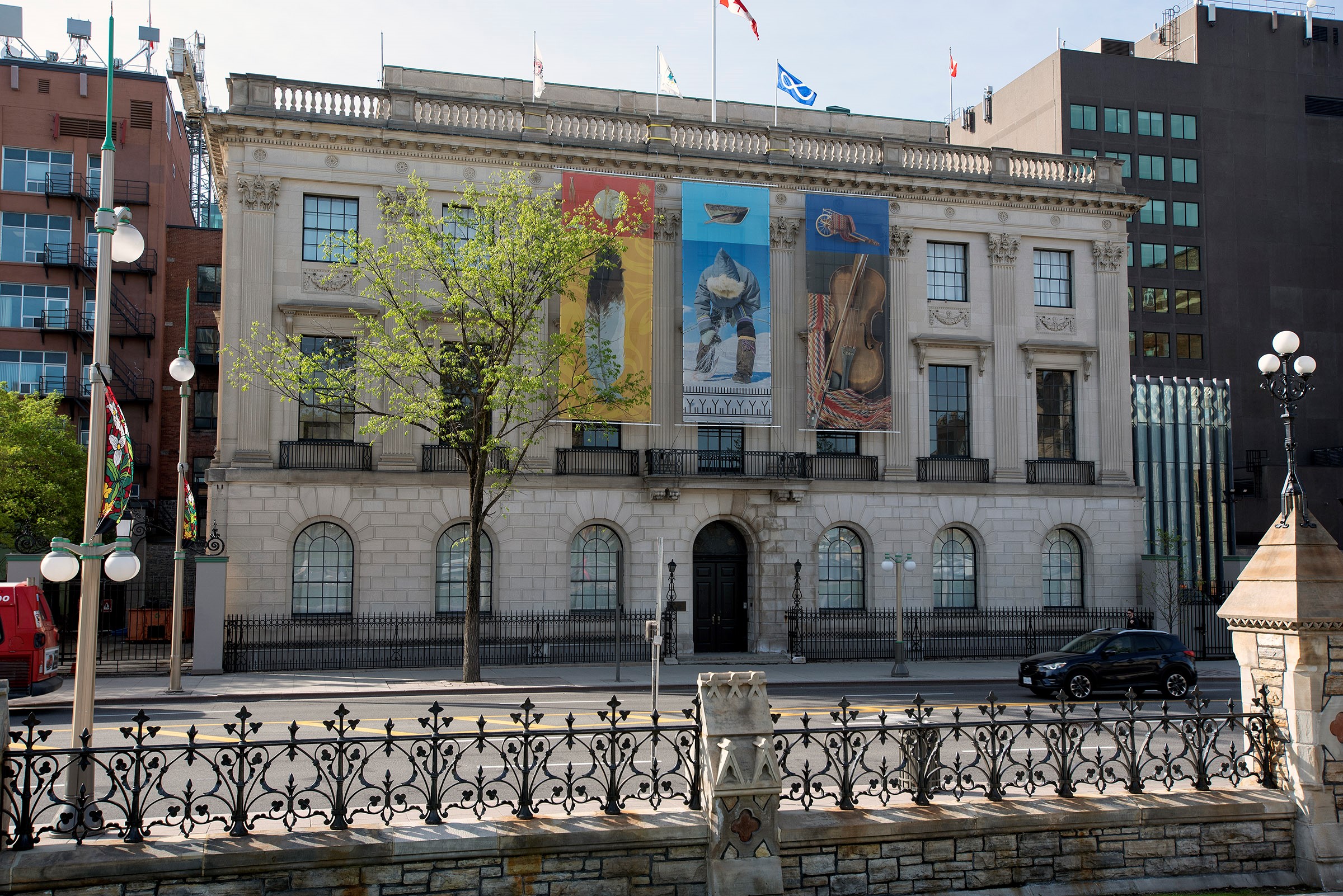 View enlarged image of the 100 Wellington building with three banners depicting Indigenous Peoples and objects.