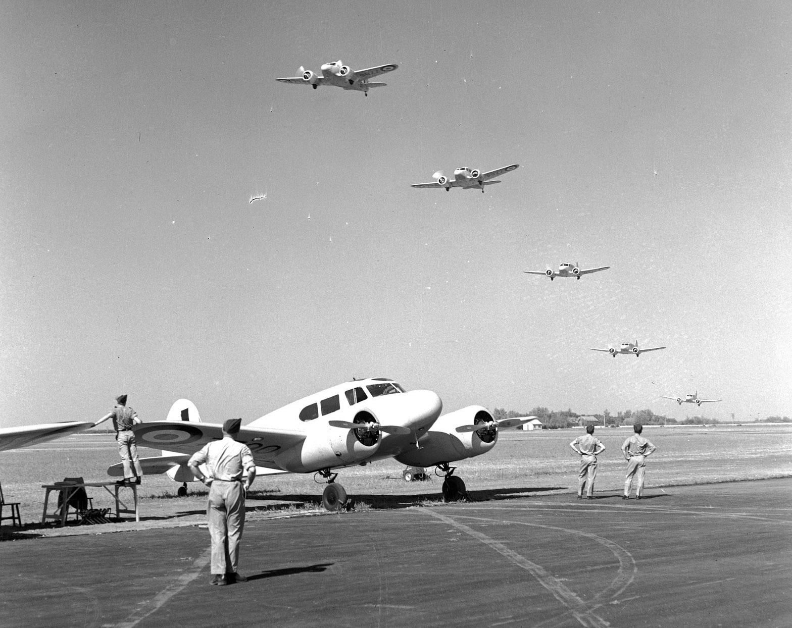 Pendant un entraînement, le 19 juillet 1941, cinq Cessna Crane de l’Aviation royale canadienne survolent en formation parfaite une piste sur laquelle se trouve un autre Crane. Ces avions bimoteurs servent à former les pilotes de bombardiers en vue de combattre les forces de l’Axe à l’étranger. PHOTO : Archives du MDN, PL-5747