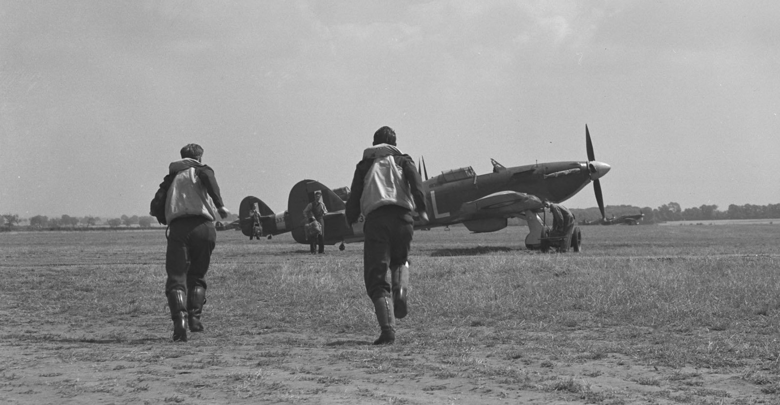 Pilots from 401 Squadron run to their Hurricane aircraft in this undated photograph. Groundcrew are waiting to help the pilots put on their parachutes and get into the aircraft. The Hurricanes could skim off the ground three minutes after an alarm was sounded. PHOTO: DND Archives, PL-4484