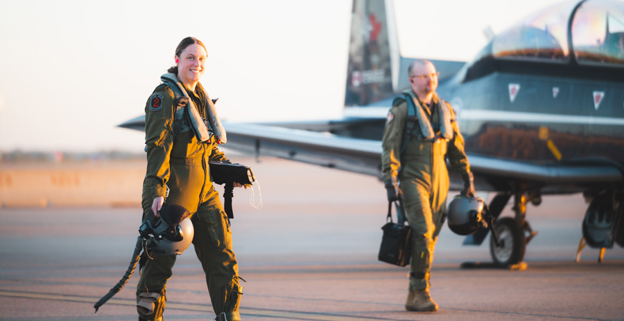 Deux pilotes portant une combinaison de vol verte et transportant des casques et des sacs traversent l’aire de trafic à côté d’un avion bleu