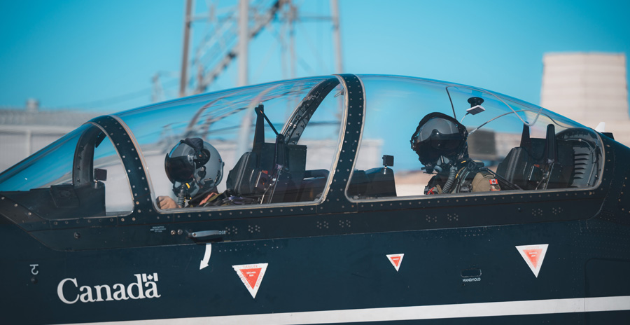 Deux pilotes portant des casques de vol gris sont aperçus dans le poste de pilotage d’un avion biplace bleu