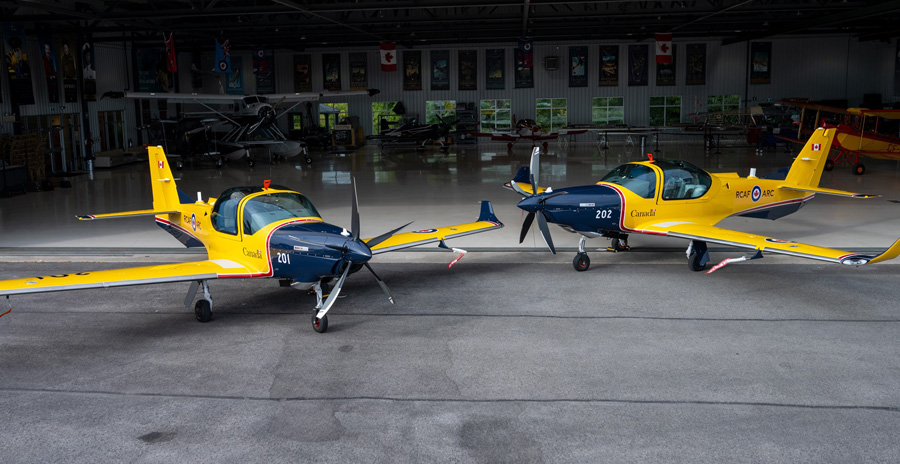 Deux avions biplaces jaune et bleu sont stationnés sur l’aire de trafic devant un grand hangar d’aviation