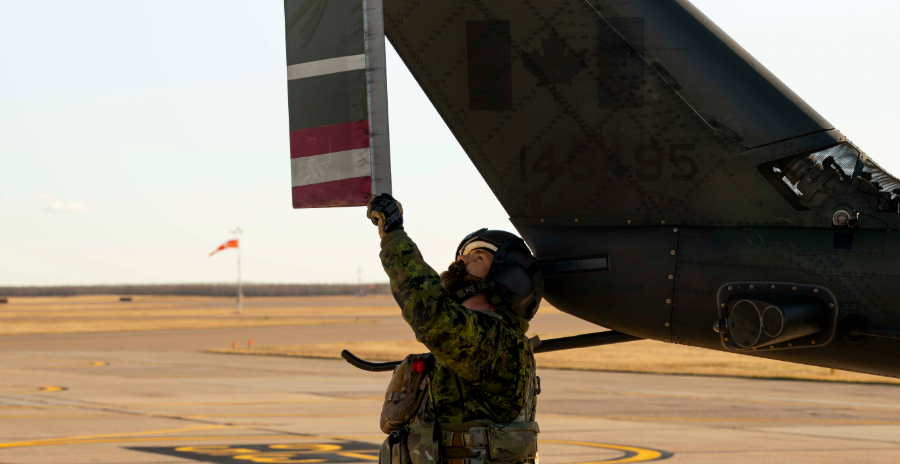 Canadian Armed Forces member performs a post-flight check and inspects the tail rotor of a CH-146 Griffon helicopter on an airfield.