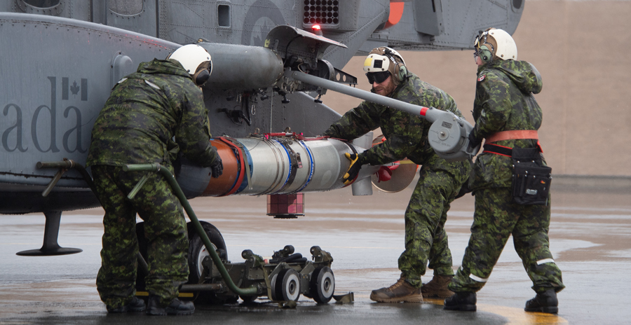Air Force technicians loading a torpedo on a helicopter.