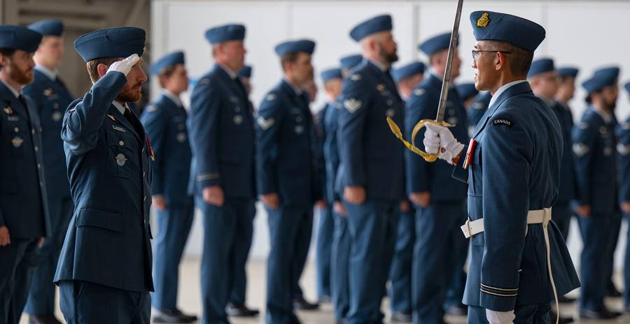 Air force personnel in blue dress uniforms stand in formation as two officers exchange a salute during a formal event.