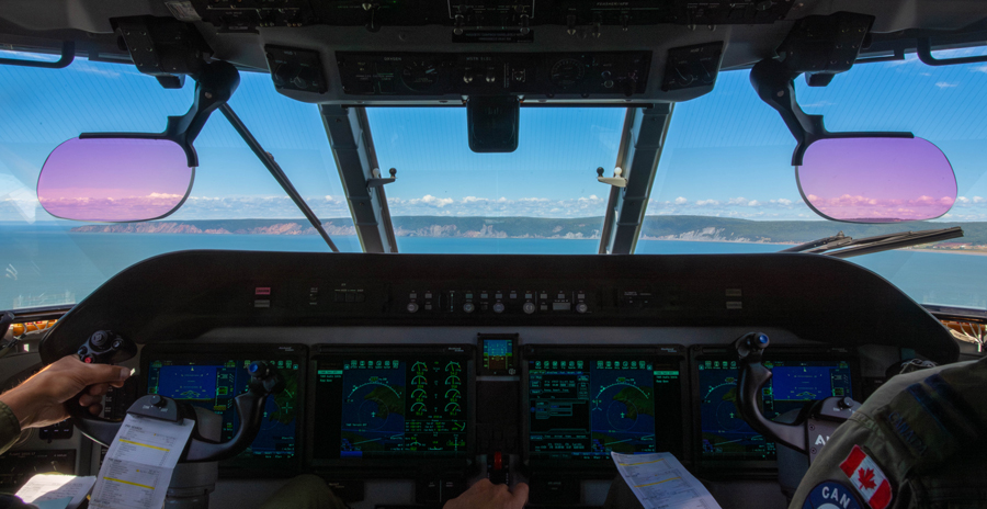 A cockpit view from an aircraft flying over a coastline with two pilots at the controls, digital flight instruments are illuminated.