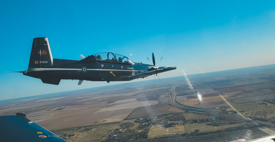 A blue, two-seat aircraft is seen flying from the cockpit of another similar aircraft.