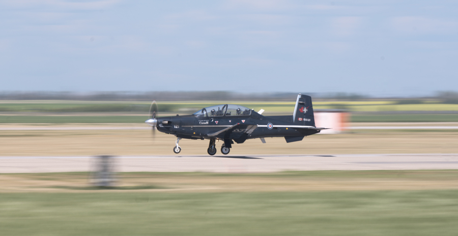 A blue two-seat aircraft is seen touching its landing gear on a runway at speed.
