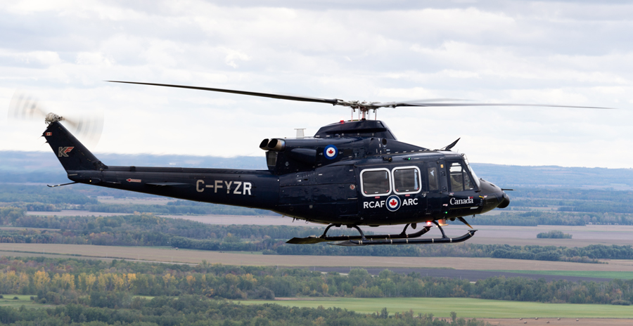 A blue helicopter in flight over fields and trees