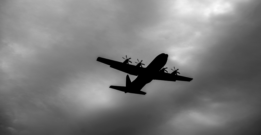 Silhouette of a CC-130H Hercules aircraft flying against a cloudy sky