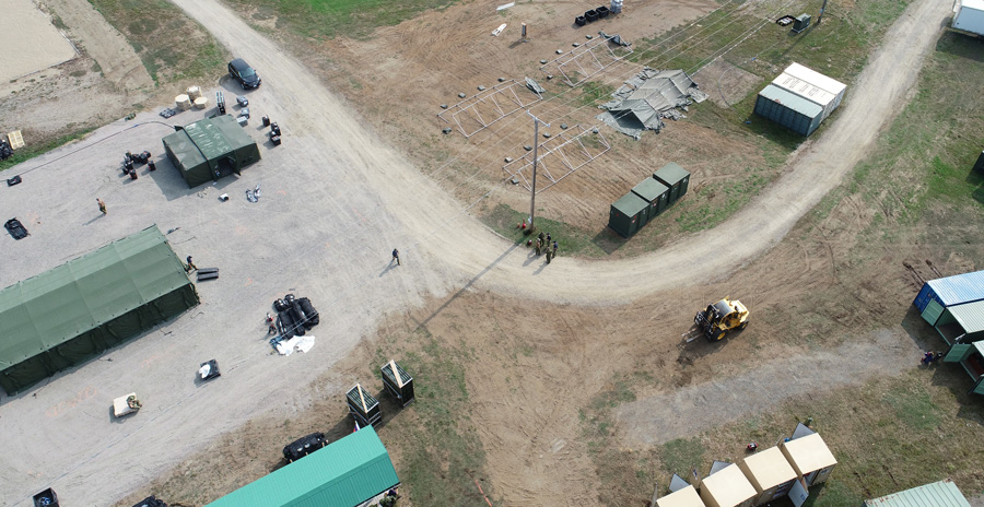 Aerial view of military personnel establishing a temporary camp with tents and equipment during an exercise.