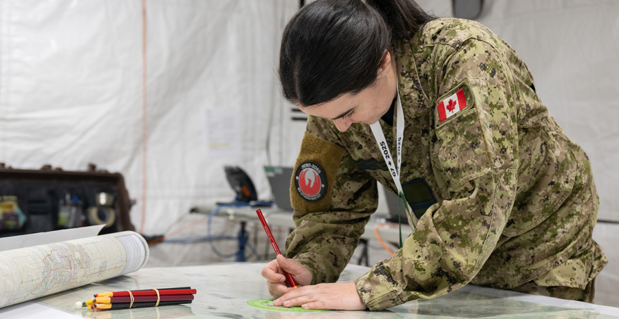 A military member conducts map marking and planning tasks during an operation using field maps and tools.