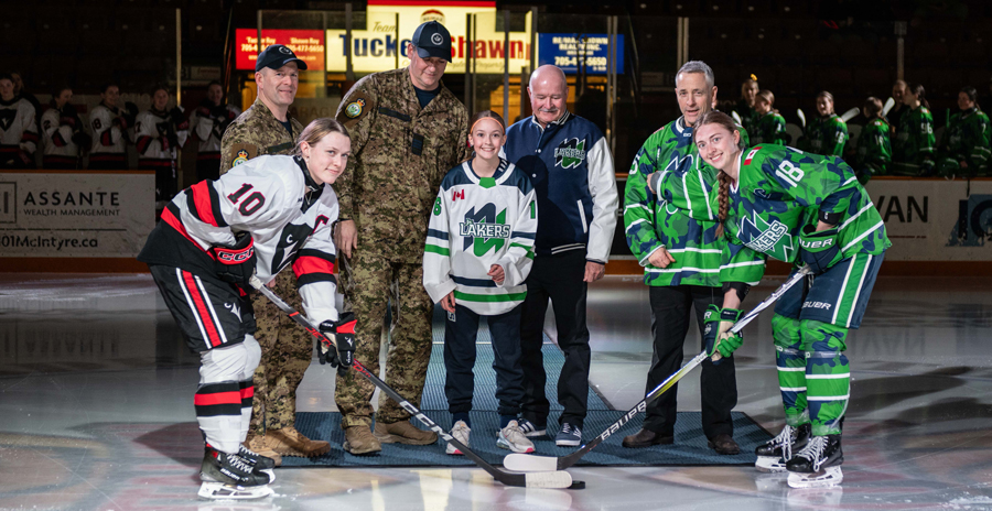 Military members and hockey players gather at center ice for a ceremonial puck drop before a game.
