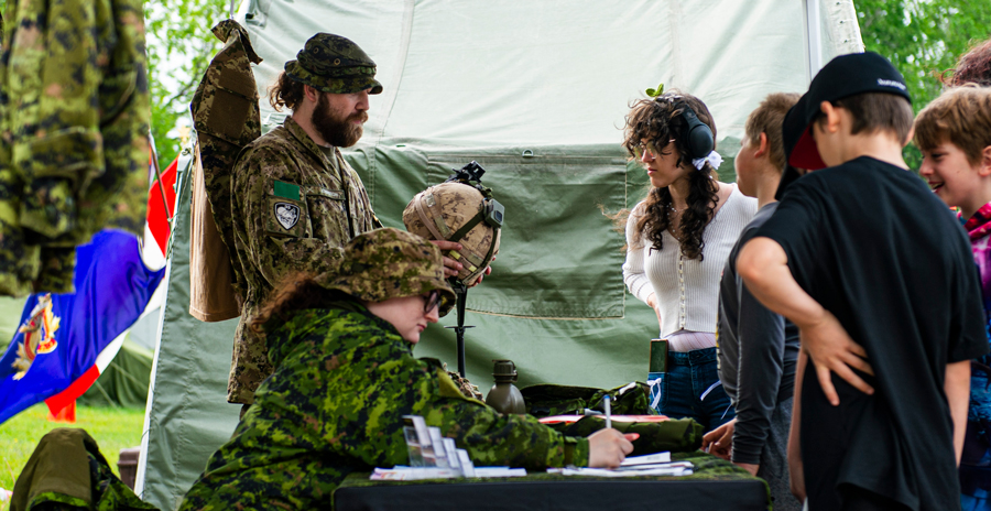 Military personnel at an outdoor booth interact with visitors, displaying gear and providing information.