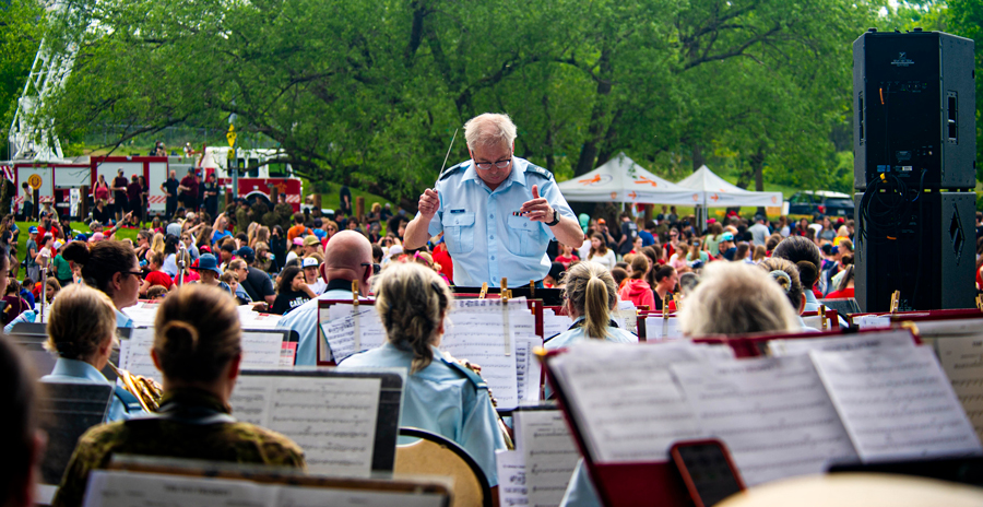 A military band performs at an outdoor event with a large crowd.