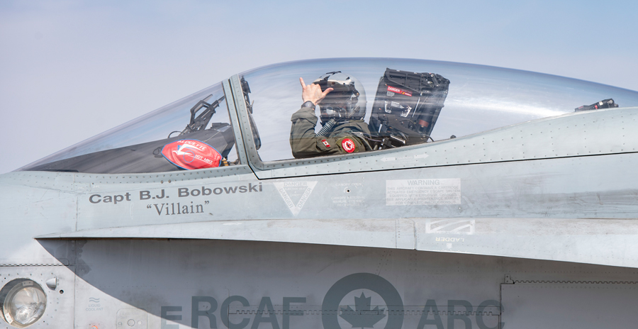 Close-up of a fighter jet cockpit with a pilot inside, and visible markings on the aircraft.