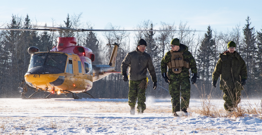 An RCAF helicopter with red and yellow markings on a snowy field, with three uniformed members of the Canadian Armed Forces walking away from it.