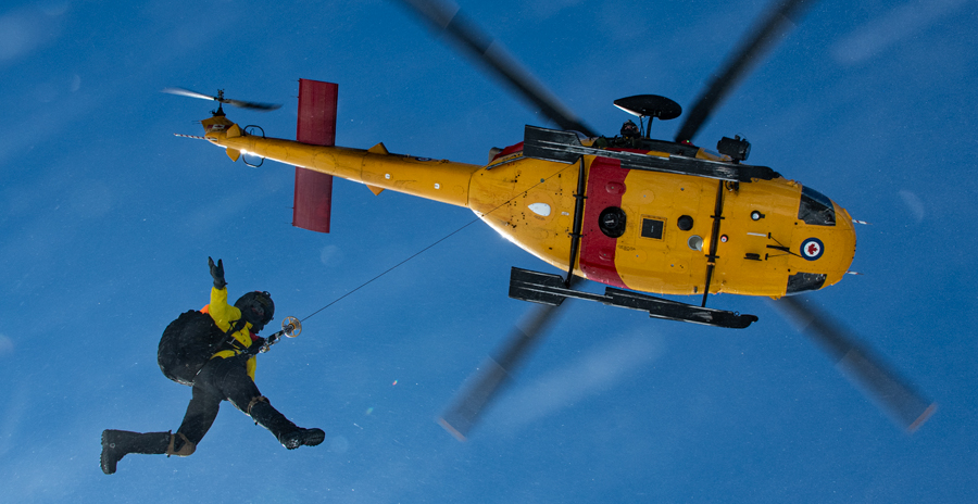 A member of the Canadian Armed Forces is lowered from a yellow and red rescue helicopter during Exercise Frozen Muskox.