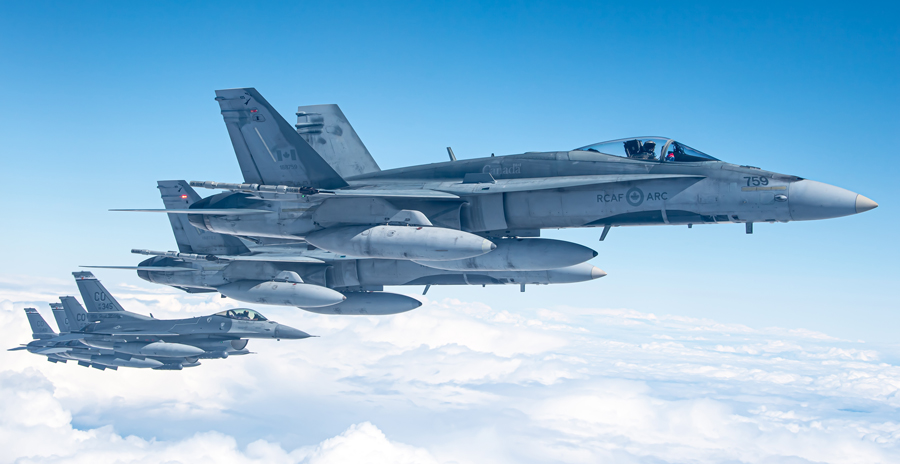 Two RCAF fighter jets with four United States Air Force fighter jets fly in formation through blue skies, above the clouds.