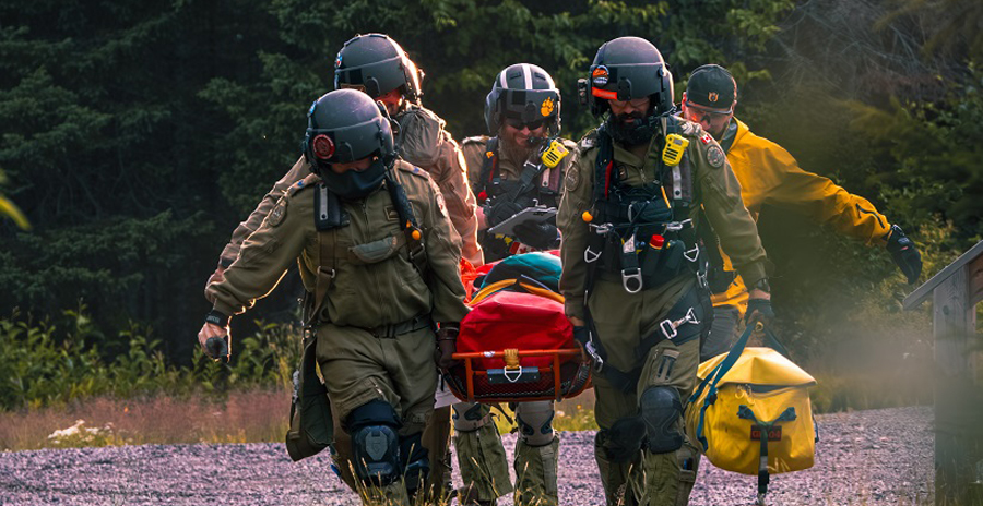RCAF members carry a stretcher on a gravel path surrounded by a wooded area.